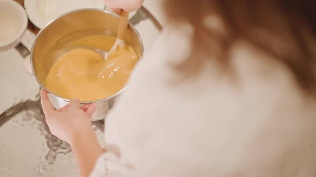 Overhead smoothing pumpkin filling into pan, soft back view of baker in white blouse, scattered plates and utensils, warm sunlight highlights glossy surface, circular strokes perfecting texture,