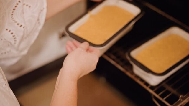 Hands placing pumpkin loaf into oven, warm spiced batter settling in rectangular pan, soft golden surface, eyelet sleeve detail, quiet morning kitchen, seasonal dessert preparation