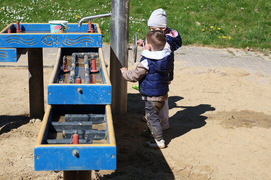 Two adorable toddlers playing together in a sandbox at a playground on a sunny day. Children enjoying outdoor activities, building and exploring with colorful toys in a safe and natural environment.