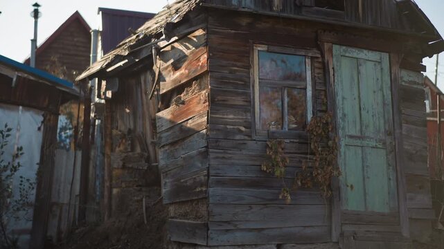Weathered wooden home exterior, peeling paint, sunlit facade, overgrown vines clinging to shutter, cracked window and sagging roofline, textured planks and flaking patina evoking melancholic rural