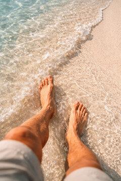 Barefoot man walking along sandy beach edge with waves