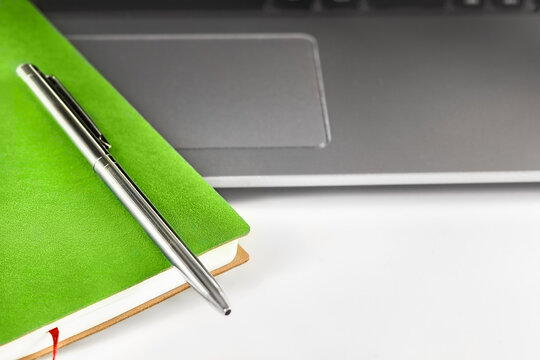 Minimalist desk or study space with laptop, green notepad and metal pen.