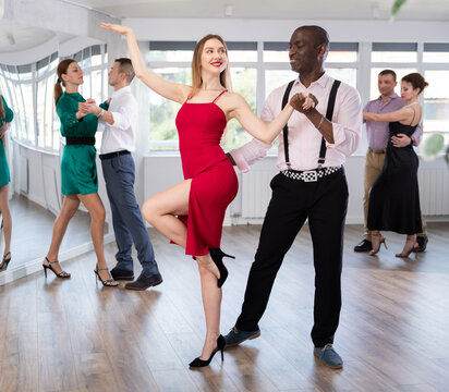 Dynamic young female and male attendees of dancing courses doing waltz in group