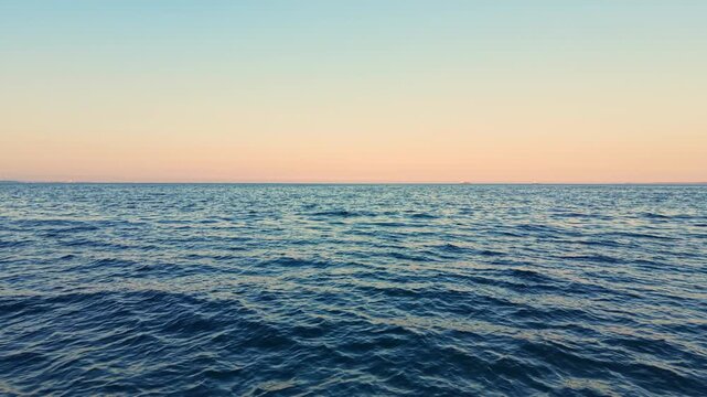 Waves roll in the ocean as the day ends. The sky shows colors changing from blue to orange and pink. The scene looks peaceful as the sun sets on the water.