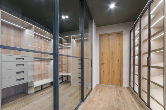 A modern dressing room with illuminated wooden shelves, drawers and glass partitions. A well-organized functional space.