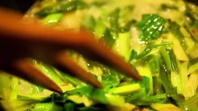 Cooking wild leek asphodelus greens in pan. Macro shot of traditional healthy vegetarian meal preparation using fresh seasonal mountain herbs for rustic culinary content