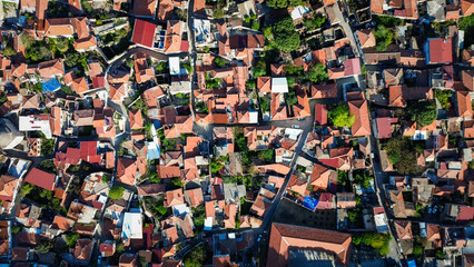 Fototapeta premium Aerial drone view of Bergama, Izmir, Turkey, showing dense urban neighborhoods, red-roofed houses, surrounding farmland, hills, and a wide Aegean landscape.