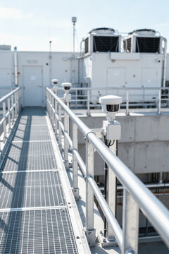 Security sensors line rooftop walkway at industrial facility with metal railings