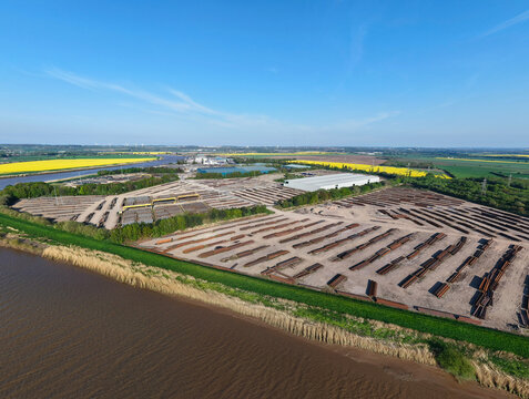 Aerial view of the PD Ports industrial storage facility with stacks of materials near the riverbank and yellow fields in Scunthorpe, England, United Kingdom.