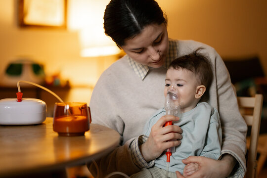 Mother gently helps baby breathe using nebulizer in warm cozy home setting