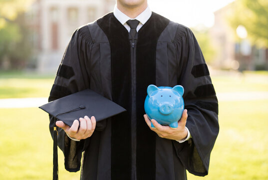 Graduate in a cap and gown holding a piggy bank to represent saving for tuition fees
