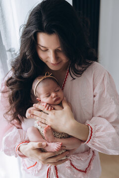 Mother holds newborn baby gently in soft morning light, peaceful and loving moment