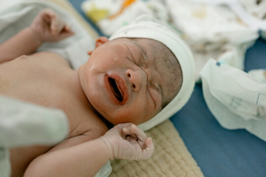 Newborn baby cries softly in hospital bed wrapped in blanket with eyes closed and fists curled