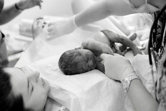 Newborn baby rests on mother&rsquo;s chest as medical staff gently care for tiny hands and feet in hospital room