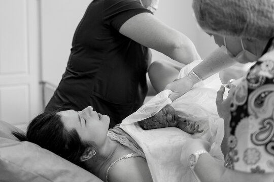 Newborn baby rests peacefully in arms of mother after birth as caregivers tend to her with care