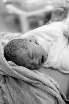 Newborn baby sleeps peacefully wrapped in soft blanket on mother's chest after birth