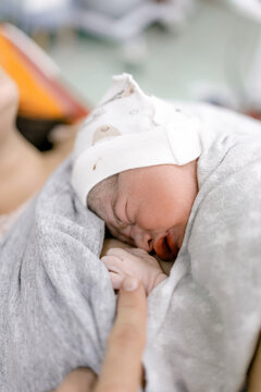 Newborn baby wrapped in soft blanket sleeps peacefully while tiny hand rests gently on adult's finger