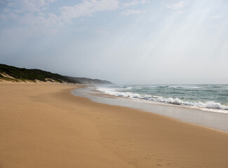 Wide sandy beach with ocean waves under cloudy sky in peaceful coastal landscape and natural seaside scenery