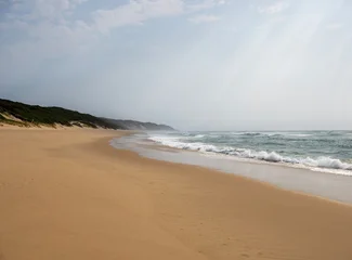 Fototapeten Küste Wide sandy beach with ocean waves under cloudy sky in peaceful coastal landscape and natural seaside scenery  © ClaudioArnese