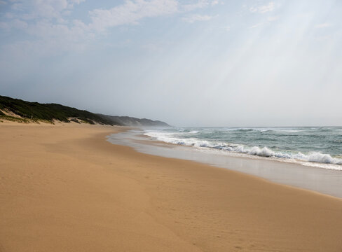 Wide sandy beach with ocean waves under cloudy sky in peaceful coastal landscape and natural seaside scenery