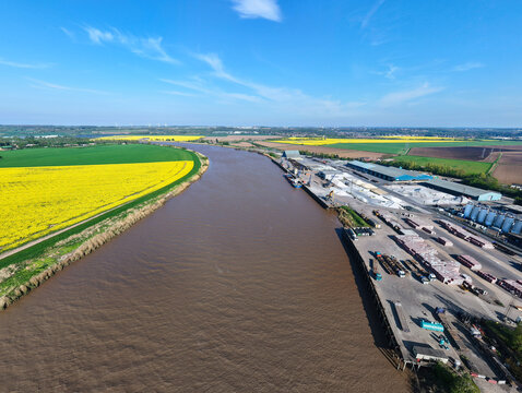 Aerial view of PD Ports industrial facility along the River Trent with yellow rapeseed fields and green farmland under a blue sky Scunthorpe, England, United Kingdom.