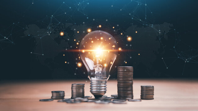 Innovation and financial growth concept. Glowing light bulb surrounded by stacked coins with digital world map background. Investment strategy, ideas, global economy and modern technology success.