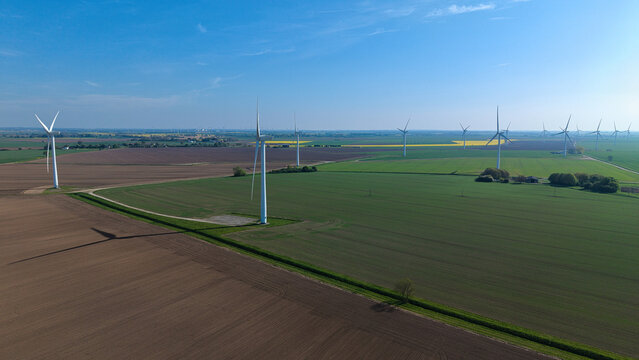 Aerial view of white wind turbines standing in vast green and brown agricultural fields under a clear blue sky in Eastoft, England, United Kingdom.