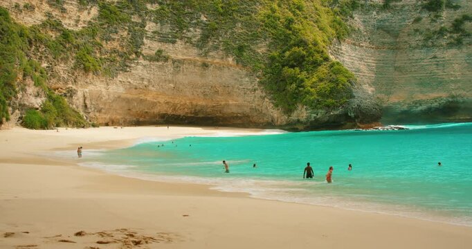 People swim in turquoise water near sheer cliffs on Kelingking beach Nusa Penida Bali