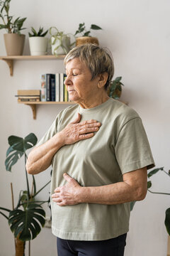 Senior woman at home with eyes closed, focusing on deep breathing and mindfulness for wellness and emotional balance. Comfortable rest, mindful happiness.