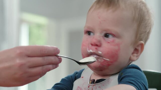 A sweet, yet slightly messy, food-stained toddler sits happily in a high chair, eating, a clear demonstration of the pure joy and inevitable mess that comes with mealtime