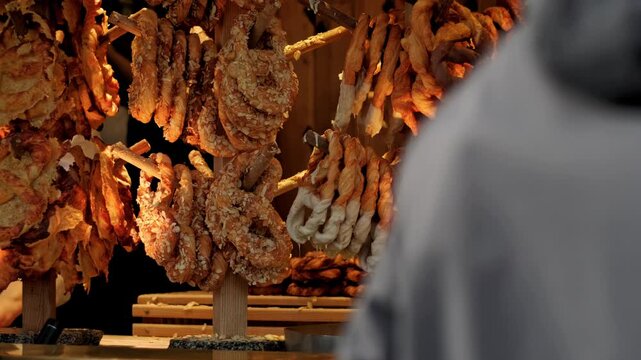 Baker displaying assorted puff pastry treats on a wooden rack. Freshly baked pretzels and twisted dough sticks with nuts and white glaze for catering service.