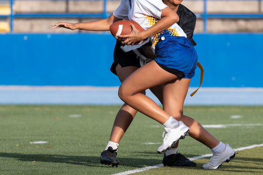 Female flag football player running with the ball during a fast-paced game.
