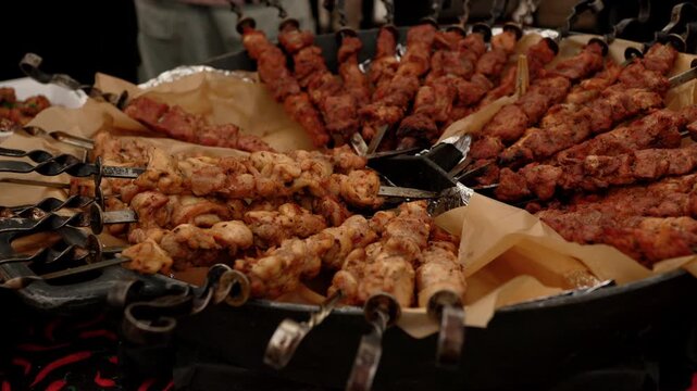 Grilled meat skewers arranged in circular pan. Chef serving assorted kebabs for outdoor catering. Roast barbecue food preparation process for festive event meal.