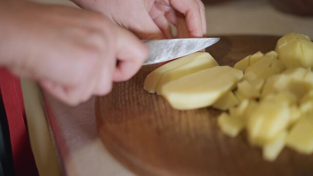 Instructional closeup slicing potato on board, steady pace, paring knife technique, precise fingertip tuck, veteran home cook demonstrating method, warm kitchen light, neatly diced pile