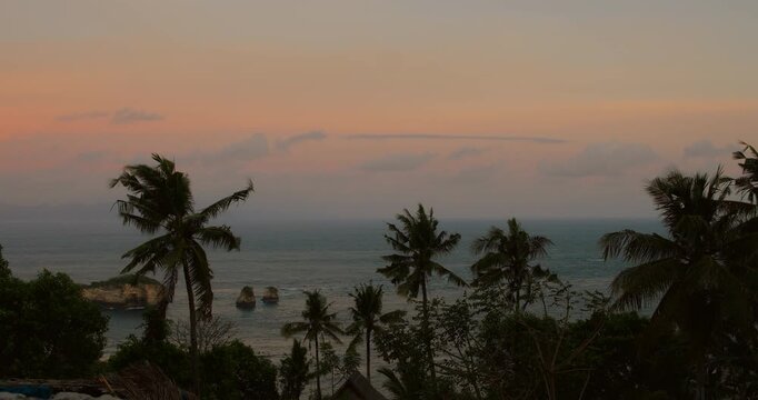 Tropical ocean view from Nusa Penida cliff at sunset with palm trees and rock islands