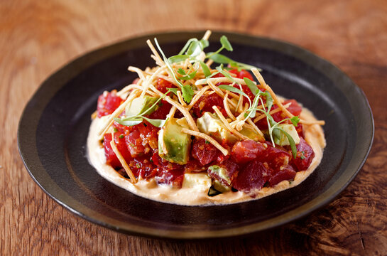 Tuna Ceviche taco on a soft shell tortilla topped with micro greens and avocado in a dark plate on a wooden table