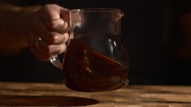 Aerating coffee in glass server, swirling liquid, light reflections and shadows, artistic coffee preparation.