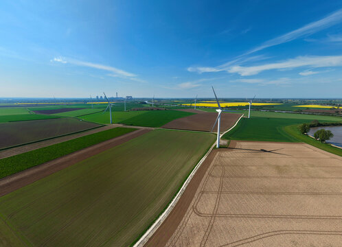 Aerial view of Airmyn Wind Farm with white turbines standing in patchwork agricultural fields under a clear blue sky Airmyn, England, United Kingdom.