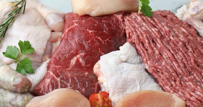 Different raw meat products and spices on light grey table, closeup. Camera moving right