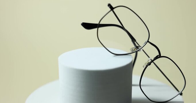 Pair of stylish eyeglasses on podium against light background, rotating