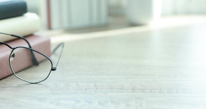 Stylish glasses and books on wooden table indoors, closeup. Camera moving right