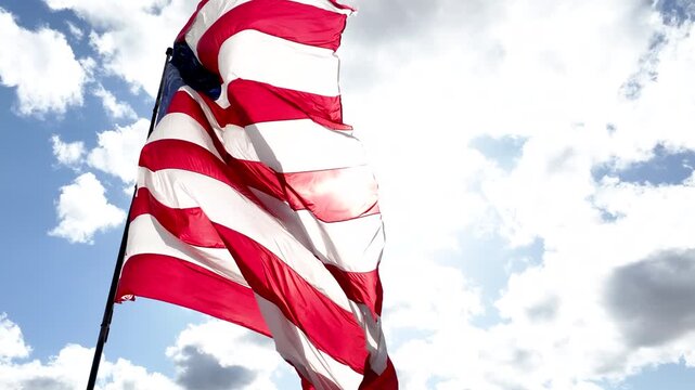 Patriotic US Flag Waving Against Blue Sky and Sunlit Clouds
