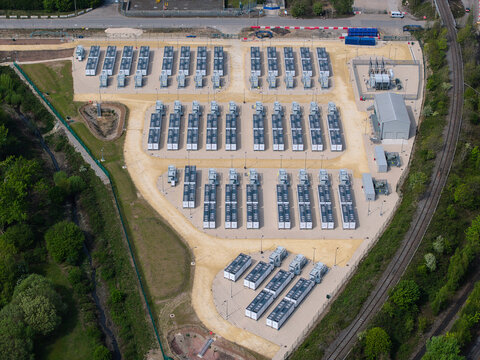 Aerial view of Battery Energy Storage Systems with rows of containerized units and electrical infrastructure surrounded by green trees in Knottingley, England, United Kingdom.