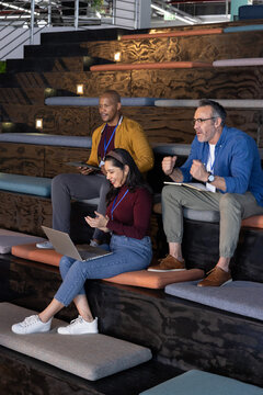 Diverse coworkers collaborating in amphitheater office wearing business clothes with laptop, tablet