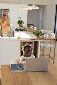 African American father and child working on laptop in kitchen at table with headphones, notebook