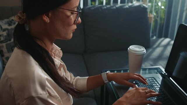 Woman working on laptop at home during daytime camera moves face to hands showing shift of focus from face to typing and concentrated workflow in home environment