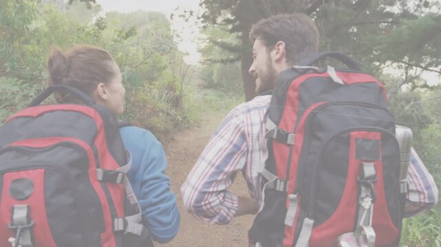 Hiking couple entering narrow trail with backpacks walking while exchanging smiles, talking for fun