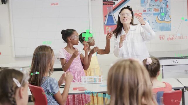 Teacher holding phone initiating science demo in lab, guiding girls comparing pink beaker