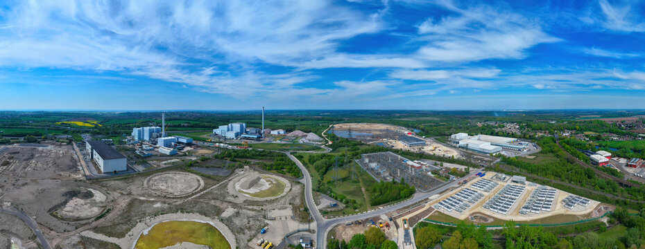 Aerial view of Battery Energy Storage Systems and industrial power facilities surrounded by green fields and construction sites under a blue sky in Knottingley, England, United Kingdom.