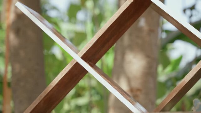 Closeup of garden woodwork detail. Carved wooden fencing with natural grain in peaceful surroundings. Intricate wooden lattice structure in tranquil garden with soft sunlight and lush greenery